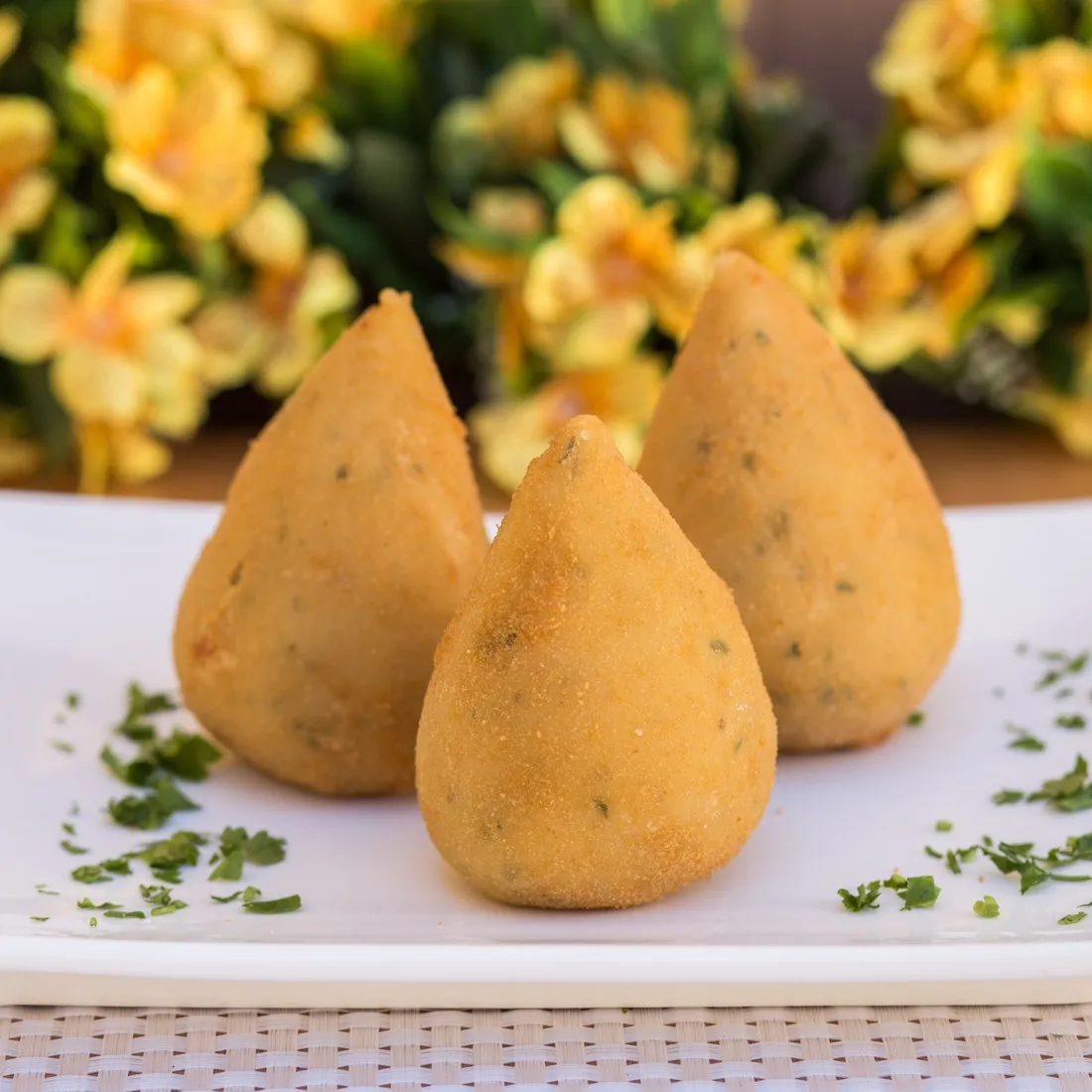 Três coxinhas douradas da Vilamore servidas em prato branco, com salsinha picada em volta.