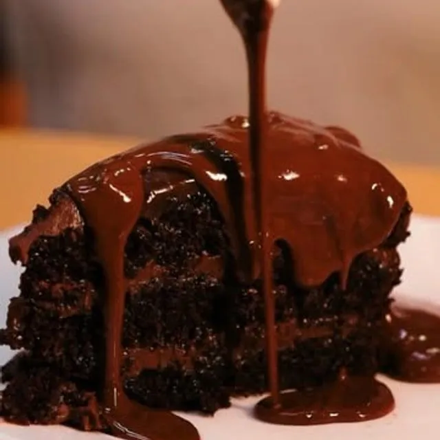 Calda de chocolate sendo despejada sobre um bolo de chocolate.