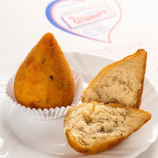 Coxinha e empada da Vilamore cortadas ao meio, servidas em pratos brancos.
