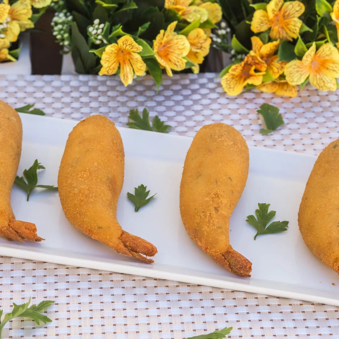 Quatro salgados de camarão com Catupiry da Vilamore alinhados em prato branco comprido.